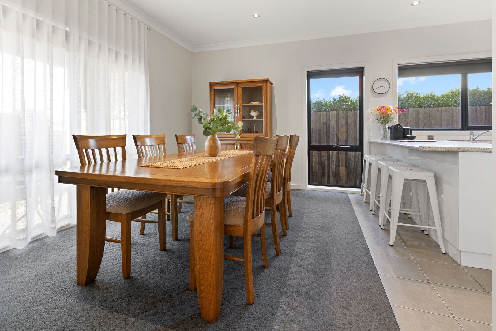 A dining area with a wooden table and chairs, a cabinet with glass doors, and a kitchen area with stools.