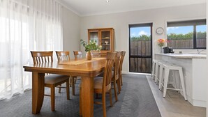 En matplats med ett träbord och stolar, ett skåp med glasdörrar och en köksdel med barstolar.