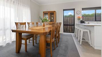 A dining area with a wooden table and chairs, a cabinet with glass doors, and a kitchen area with stools.