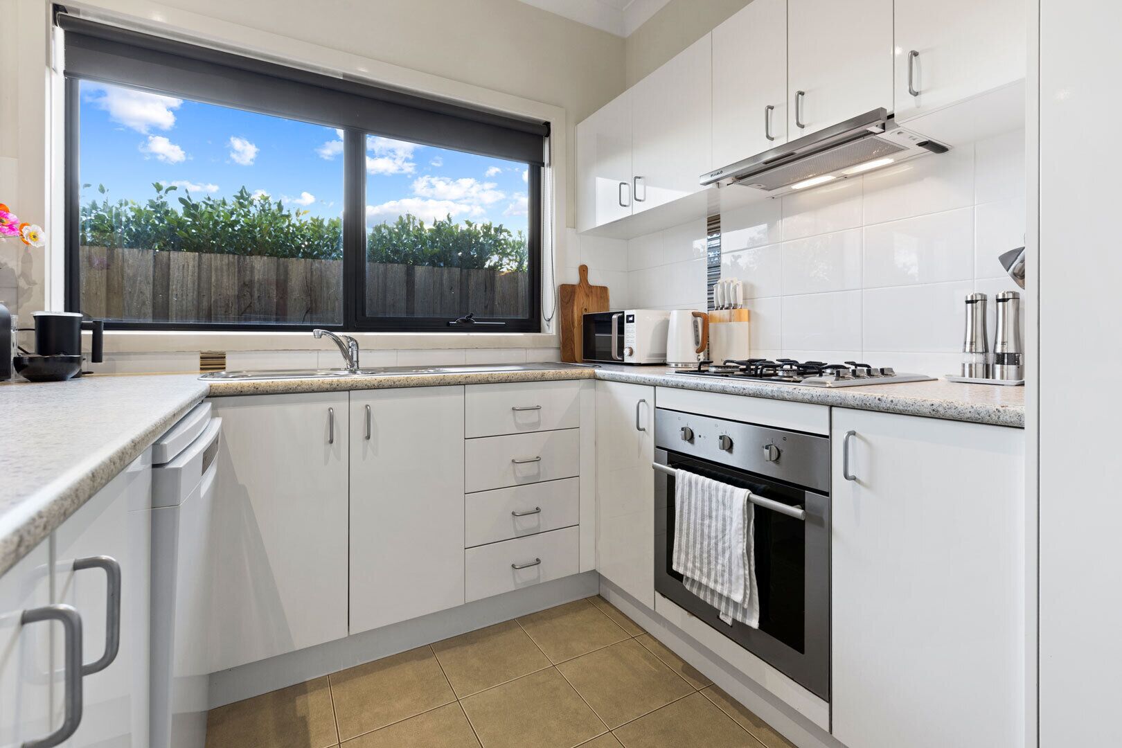 A modern kitchen with white cabinetry, a gas stove, a microwave, and a window with a view of greenery.