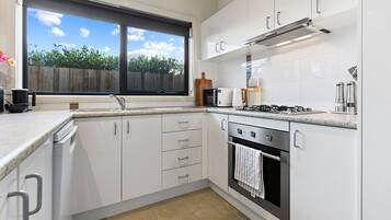 A modern kitchen with white cabinetry, a gas stove, a microwave, and a window with a view of greenery.