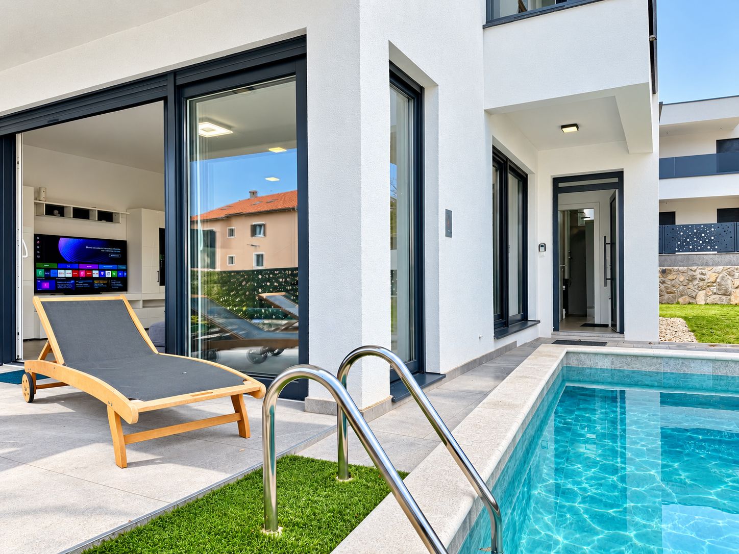 A modern outdoor pool area with a lounge chair, a poolside table, and a television screen displaying a menu.