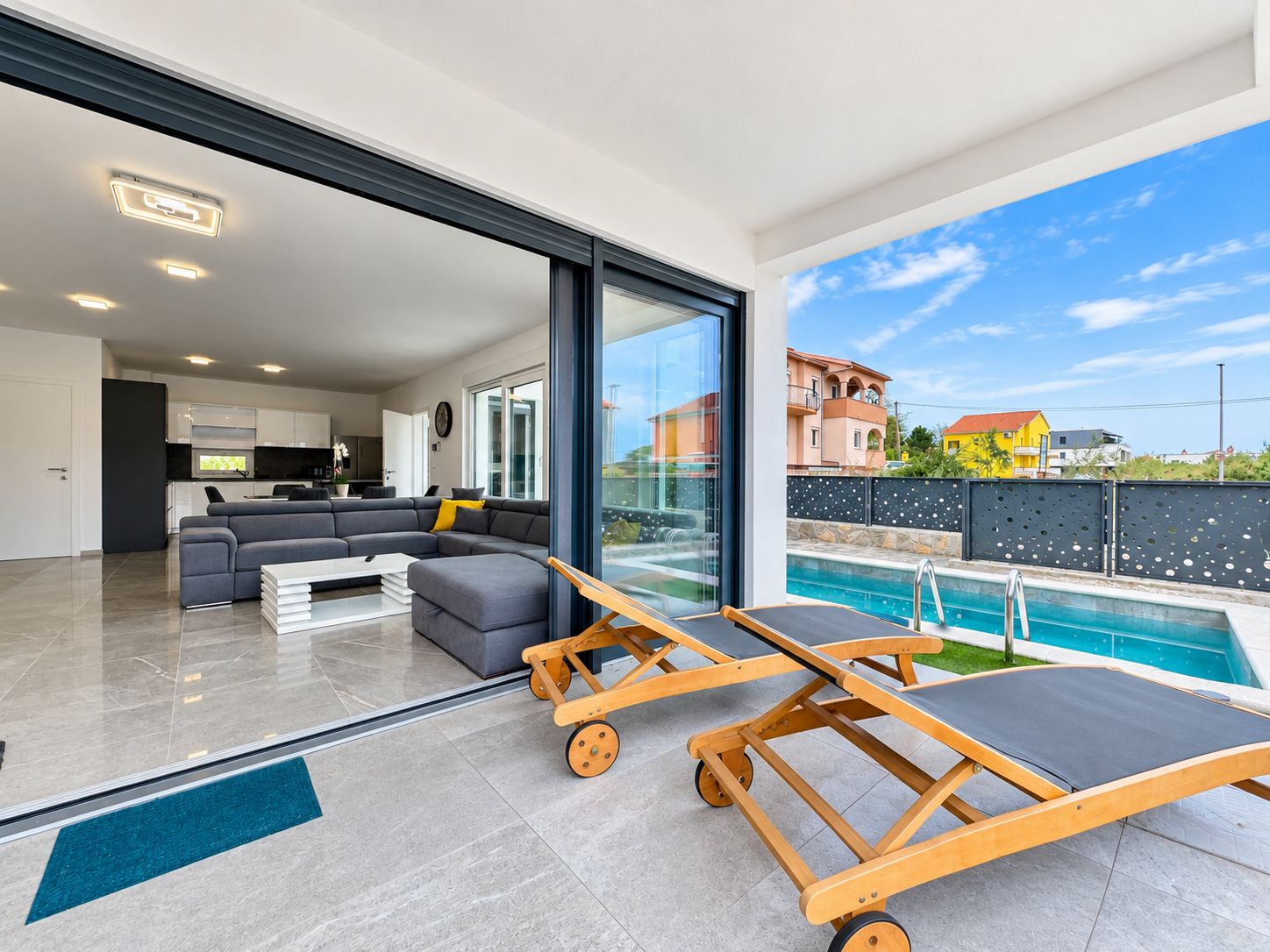 Ein modernes Wohnzimmer mit einer großen Couch, einem Couchtisch und einem Poolbereich mit Liegestühlen.