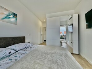 Une chambre moderne avec un lit, un tableau et une vue sur l’extérieur, visible à travers une porte ouverte.