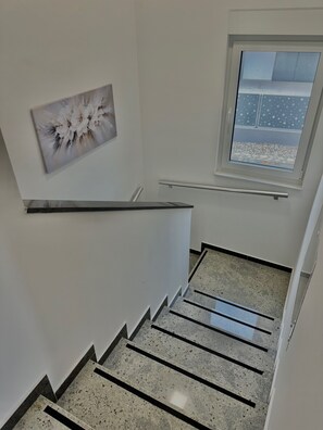 Un escalier avec une rampe, une fenêtre donnant sur un immeuble et un tableau accroché au mur.