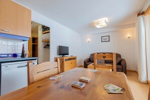 A compact living space with a kitchenette, a dining table with cards, a television, and a sofa. - Studio 4p vue montagne, ski aux pieds (Les Orres)