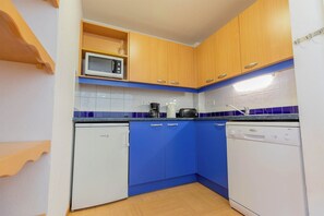 A compact kitchen with wooden cabinets, a microwave, a coffee maker, a toaster, and a dishwasher. - Studio 4p vue montagne, ski aux pieds (Les Orres)