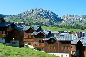 A row of wooden chalet-style buildings with sloped roofs, set against a backdrop of mountains. - Chalet Privé 10p, cheminée (Macot-la-Plagne)