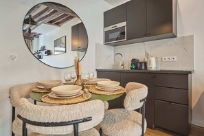 A modern kitchen with a microwave, stove, and sink. There is a dining table set with plates, glasses, and cutlery. - Apartment in the center of Paris (Paris)