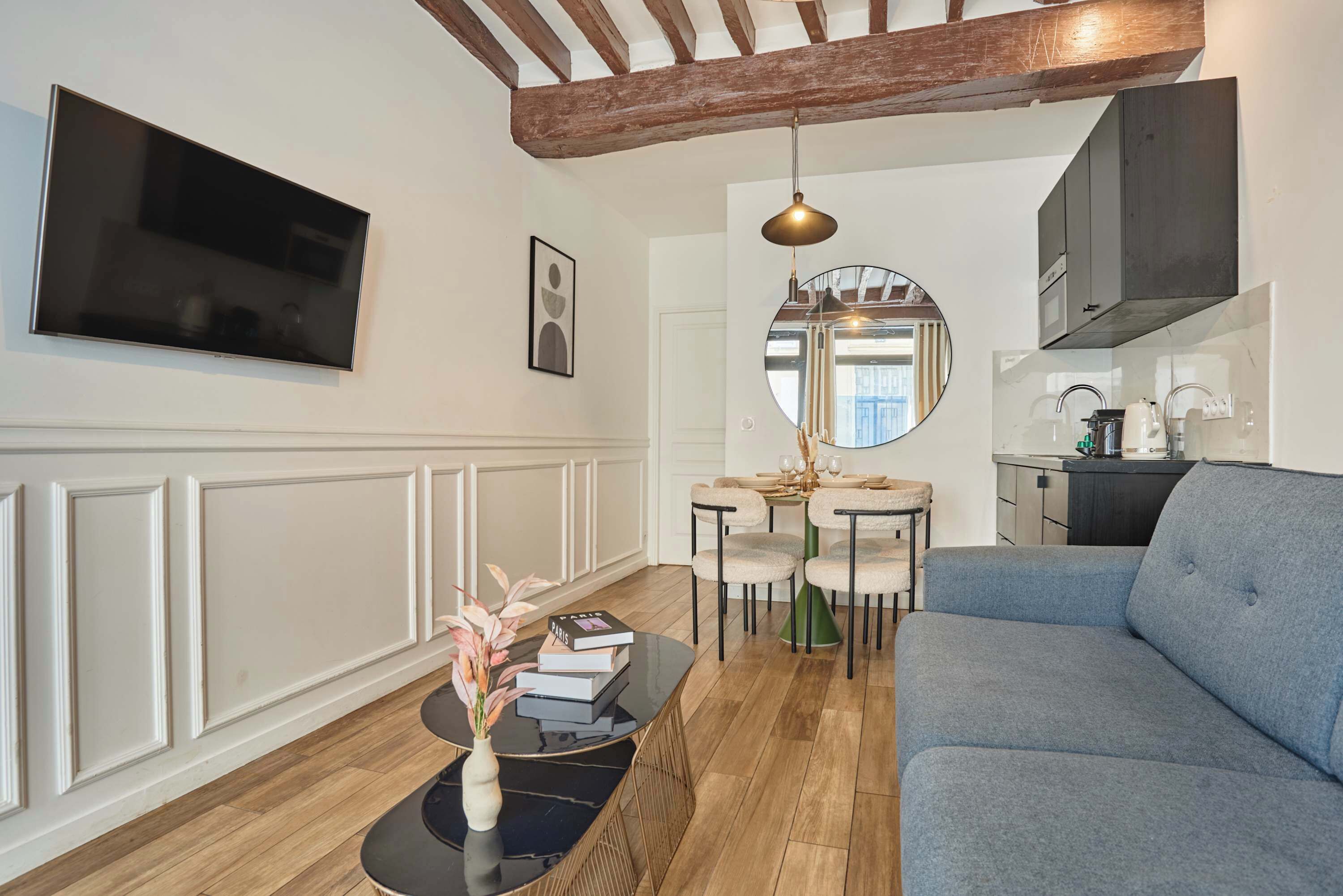 Een moderne woonkamer met een flatscreen televisie, een bank, een bijzettafeltje met een vaas, en een eethoek met stoelen en een tafel.