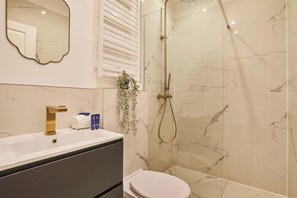 A bathroom with a marble shower, a sink with toiletries, and a toilet. - Apartment in the center of Paris (Paris)