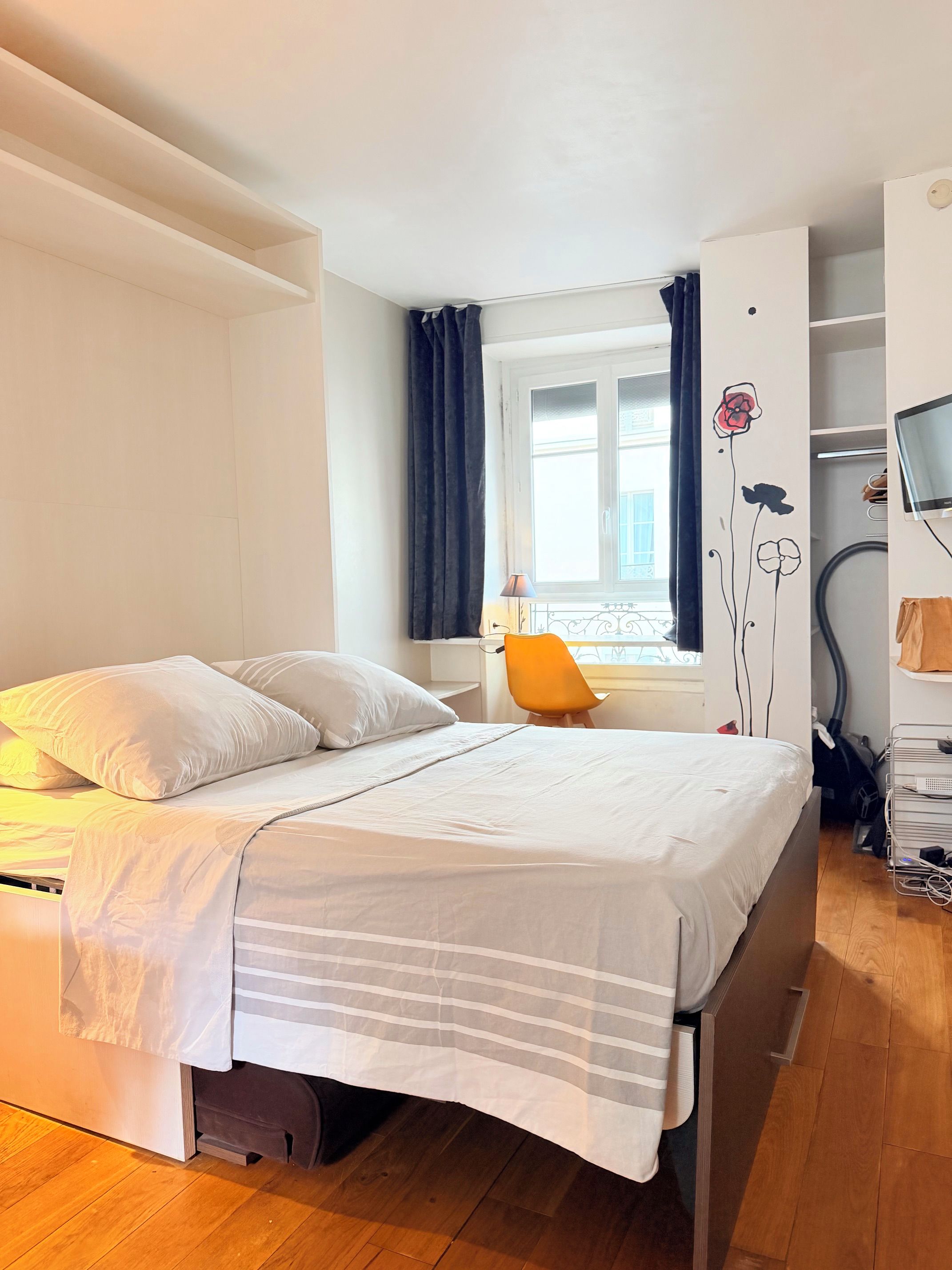Une chambre à coucher avec un lit, un bureau, une chaise, une fenêtre avec des rideaux et un téléviseur.