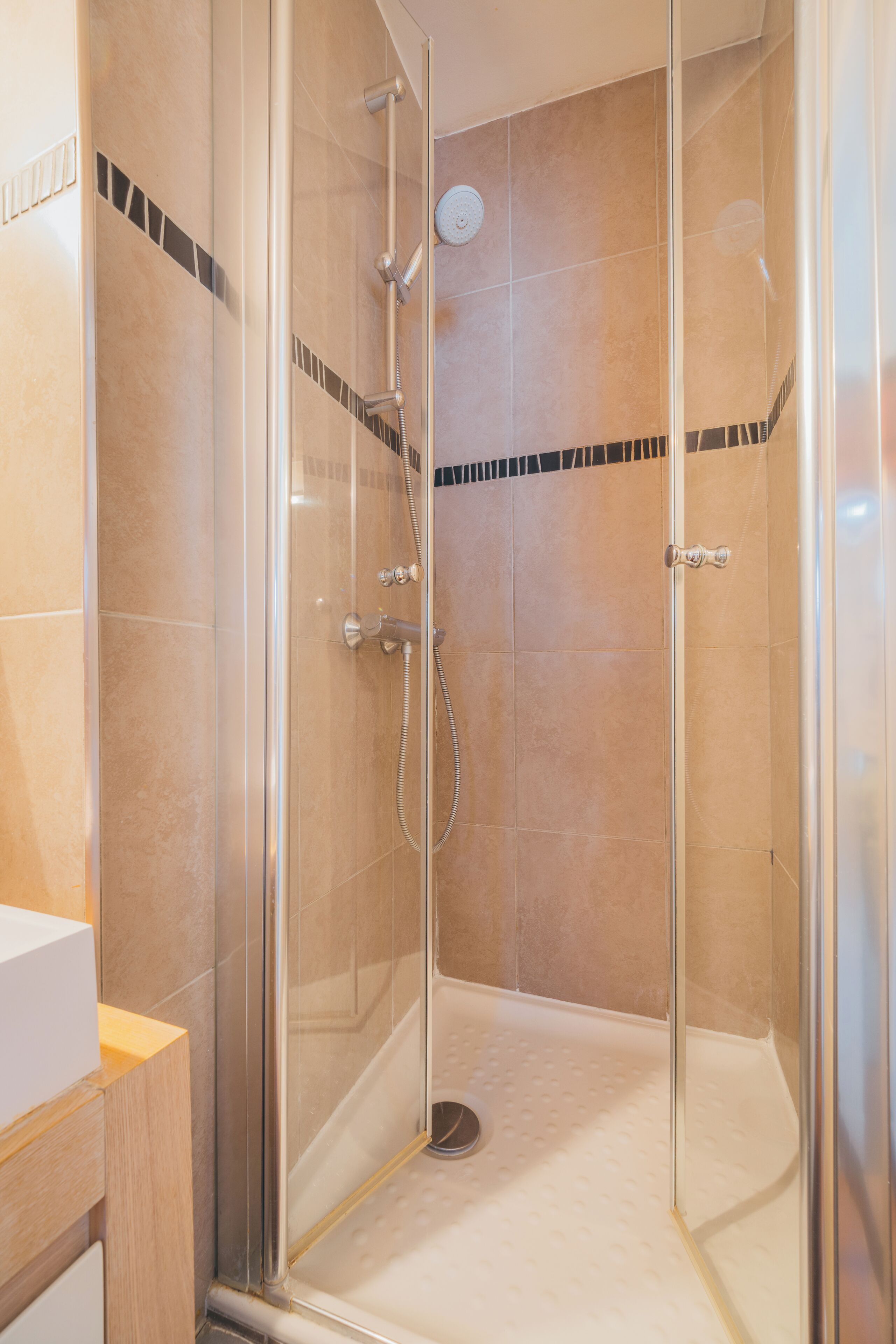 Une cabine de douche fermée par des parois en verre, dotée d’un pommeau de douche à main et d’un robinet mural.