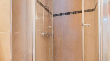 Une cabine de douche fermée par des parois en verre, dotée d’un pommeau de douche à main et d’un robinet mural.