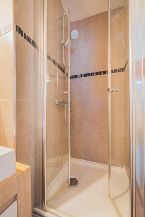 Eine gläserne Duschkabine mit Handbrause und am Wand montiertem Wasserhahn.