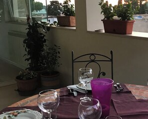 Une table avec un verre à vin, une tasse violette et une assiette ornée de motifs floraux. Des plantes en pot sont posées sur le rebord de la fenêtre.