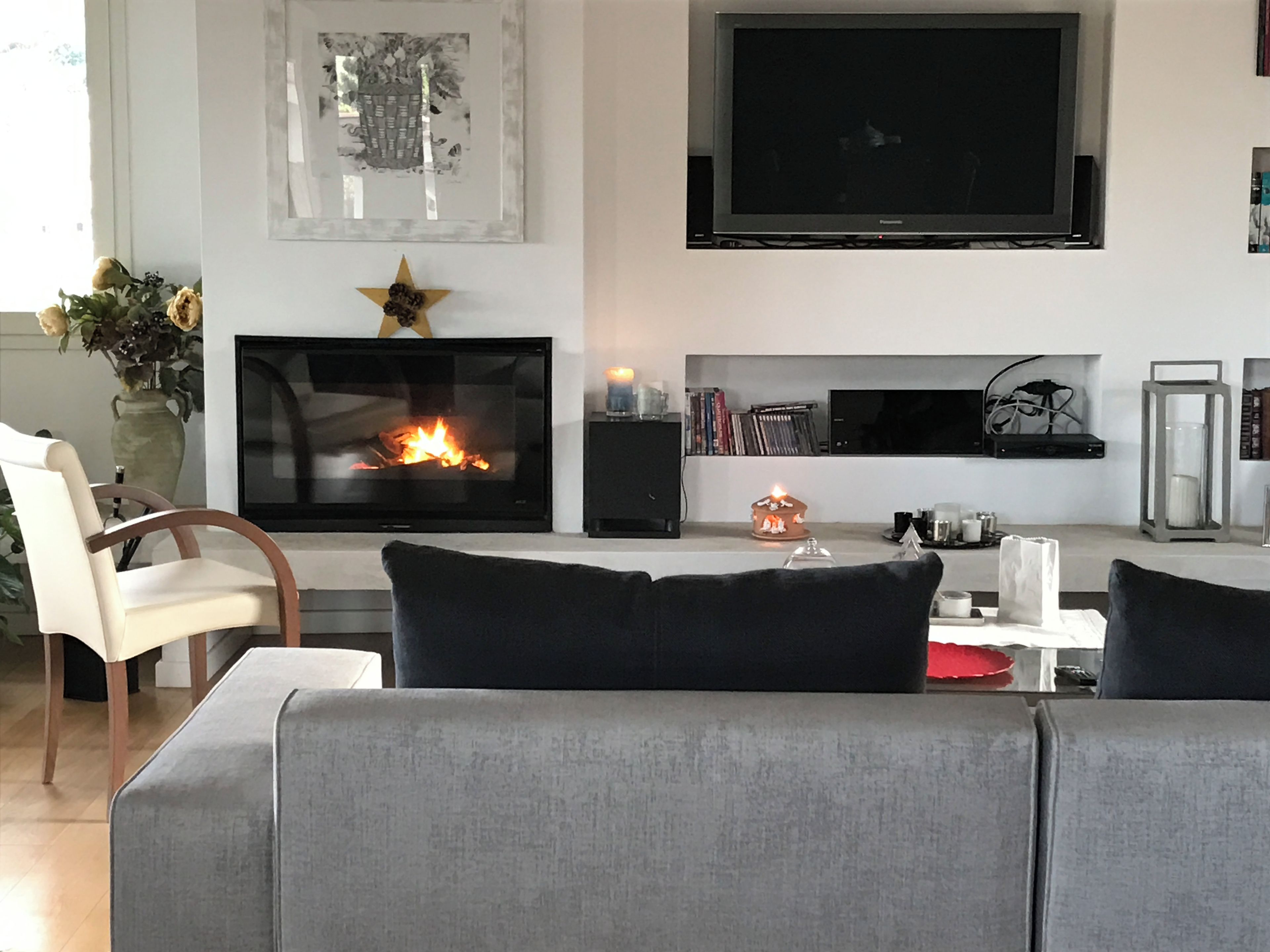 Ein Wohnzimmer mit Kamin, einem flachbildfernseher darüber und einer Couch mit Kissen.