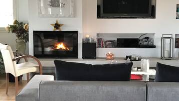 Ein Wohnzimmer mit Kamin, einem flachbildfernseher darüber und einer Couch mit Kissen.