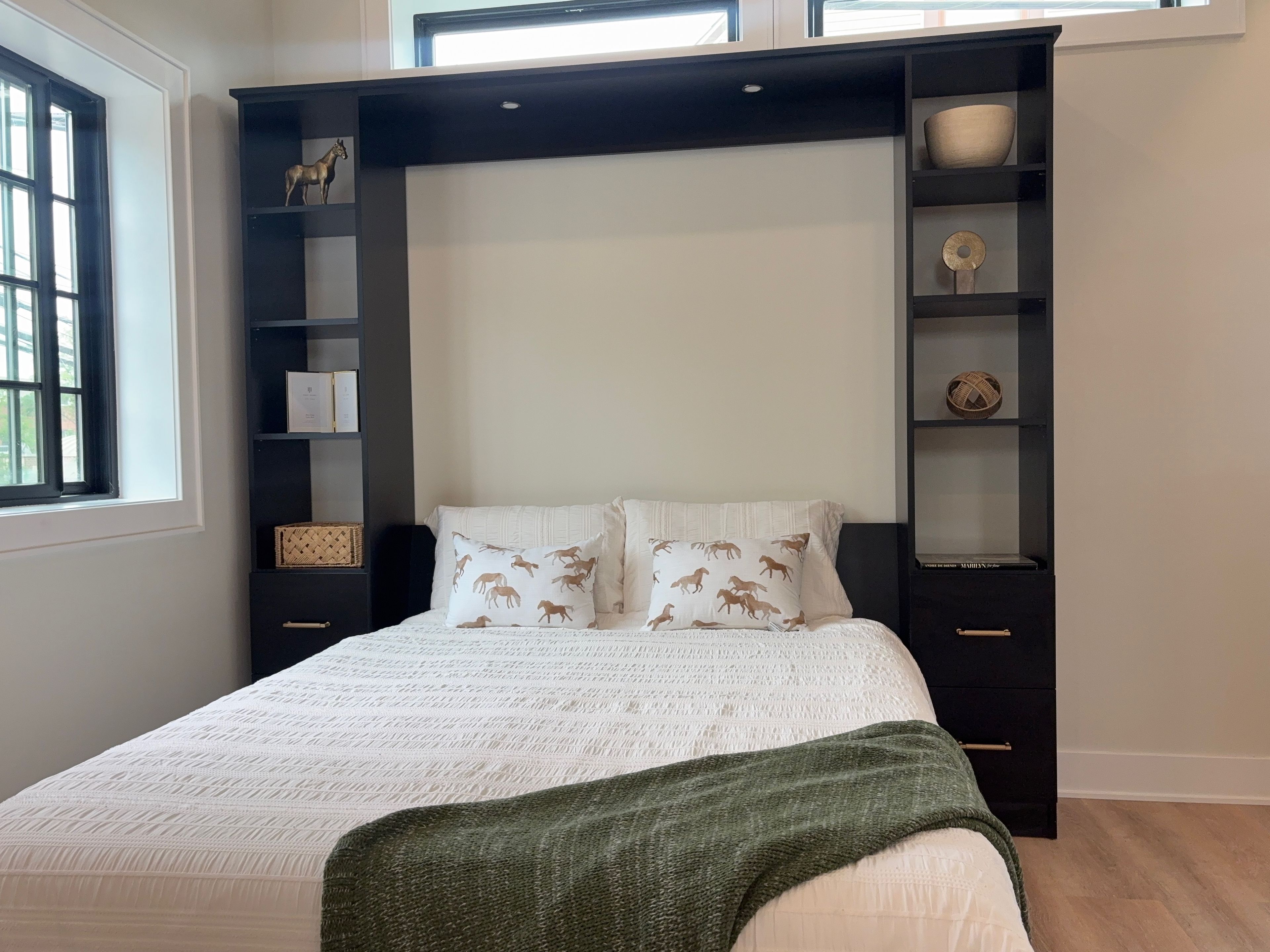 Un dormitorio con cama, ventana y estanterías empotradas con adornos.