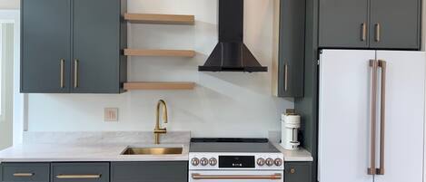 Une cuisine avec des meubles de couleur sombre, un évier en acier inoxydable, une cuisinière blanche et un réfrigérateur blanc.