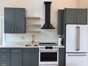 A kitchen with dark cabinets, a stainless steel sink, a white stove, and a white refrigerator. - Lux Stay in the Heart of Roscoe Village; New space with high end amenities (Chicago)