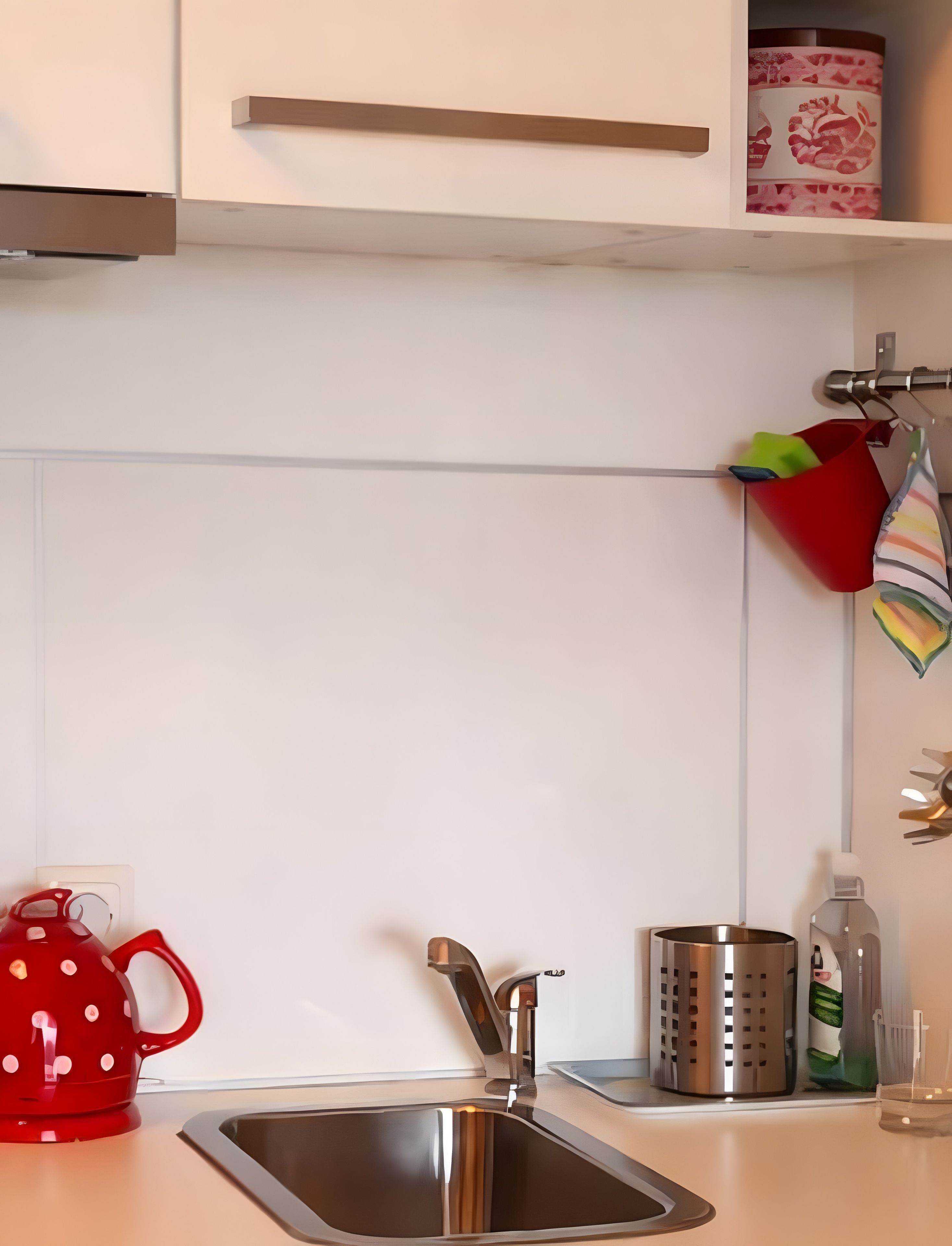 Une cuisine avec un évier en acier inoxydable, une bouilloire rouge, un récipient en métal et une casserole rouge accrochée au mur.
