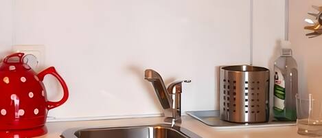 Una cocina con un lavamanos de acero inoxidable, un hervidor rojo, un recipiente metálico y una olla roja colgada en la pared.
