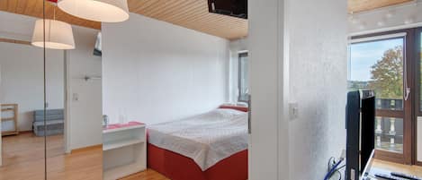 Ein modernes Schlafzimmer mit Bett, Schreibtisch, Stuhl und Fernseher.