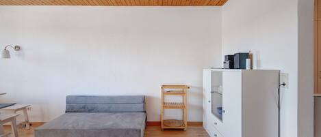 A room with a grey sofa, a wooden shelf, and a white cabinet.