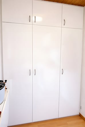 A white wardrobe with two doors and a handle, a wooden floor, and a ceiling with a wooden beam. - Apartment 'Traum Im Bayrischen Wald' with Balcony and Wi-Fi (Wiesenfelden)