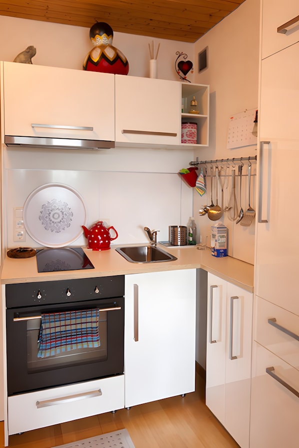 A modern kitchen with white cabinetry, a stainless steel range hood, a built-in oven, and a variety of kitchen utensils hanging on the wall. - Apartment 'Traum Im Bayrischen Wald' with Balcony and Wi-Fi (Wiesenfelden)
