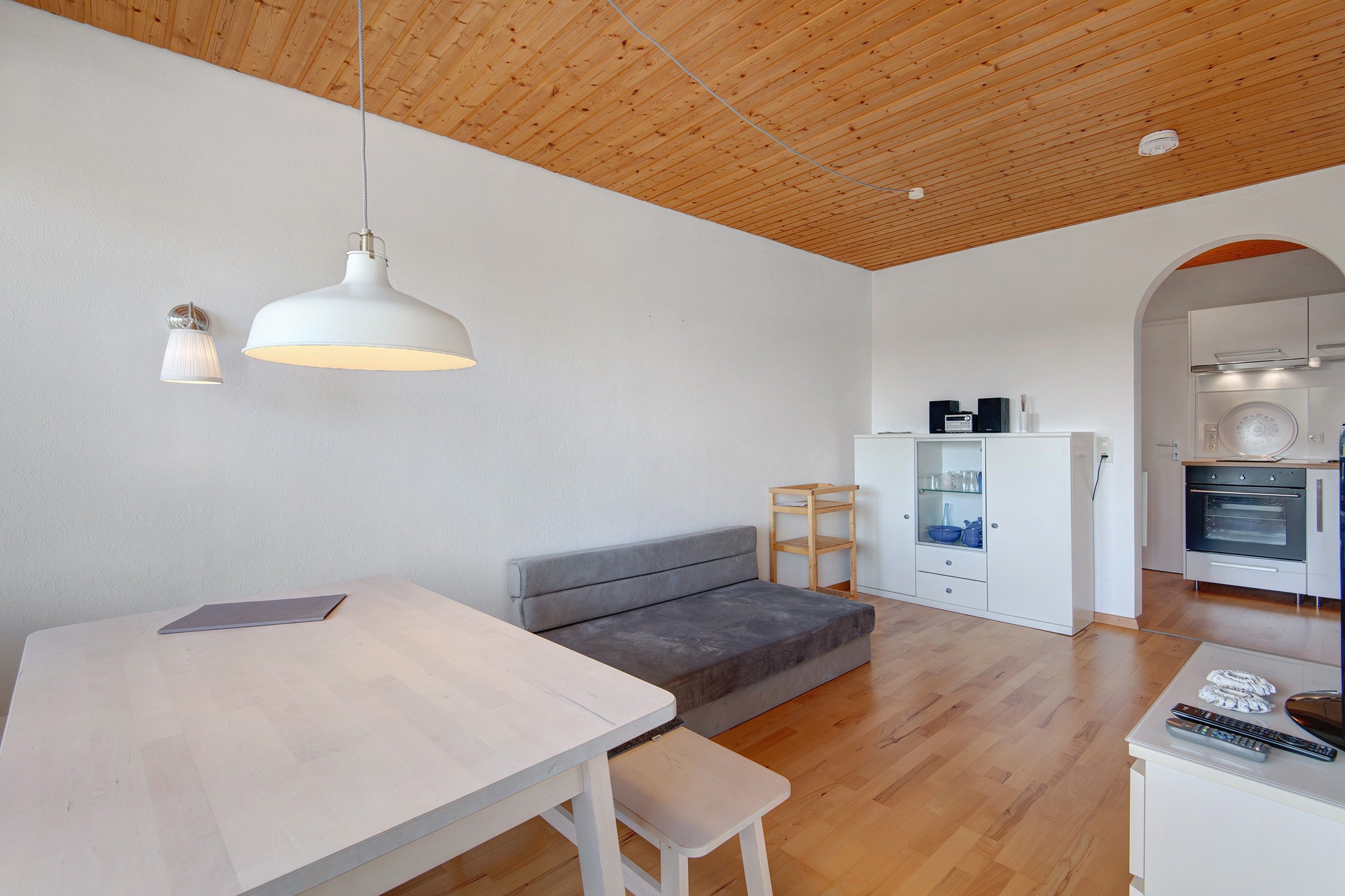 A modern kitchen with a built-in oven, a dining area with a table and bench, and a cozy seating area with a sofa.