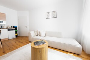A modern living room with a sofa, a coffee table, and a kitchen area with appliances. - Solentra - Popular City Location - Cozy 1BR - Free Garage (Vienna)