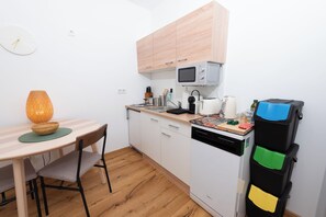 A compact kitchen with a microwave, stove, and a small refrigerator. There is a dining table with chairs and a lamp. - Solentra - Popular City Location - Cozy 1BR - Free Garage (Vienna)