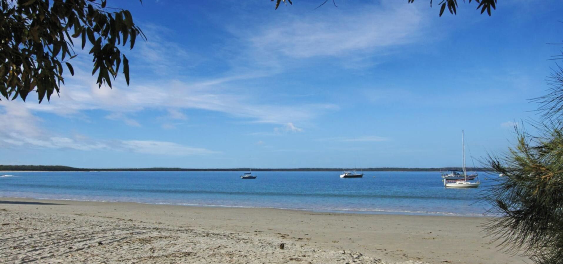 A beach with calm water, boats, and a clear sky.