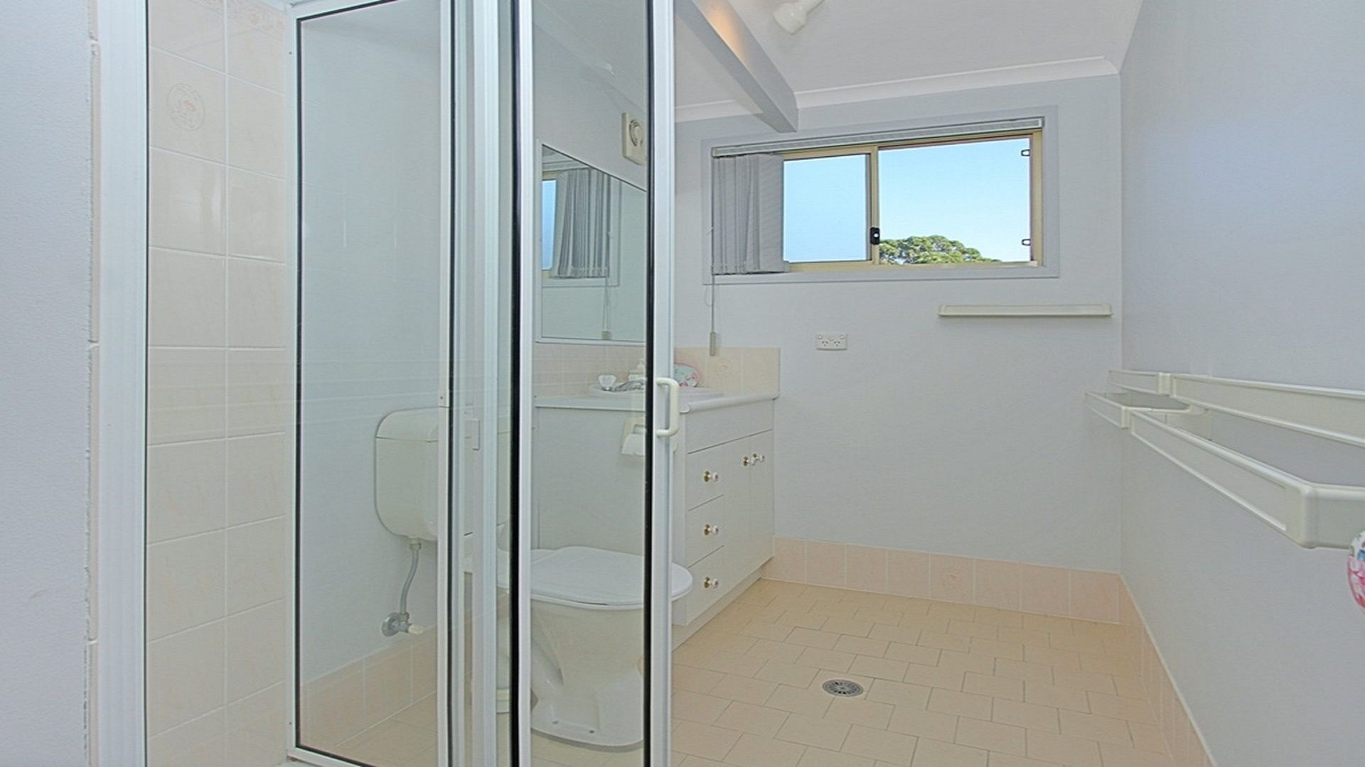 A bathroom with a glass shower enclosure, a toilet, a sink, and a window.