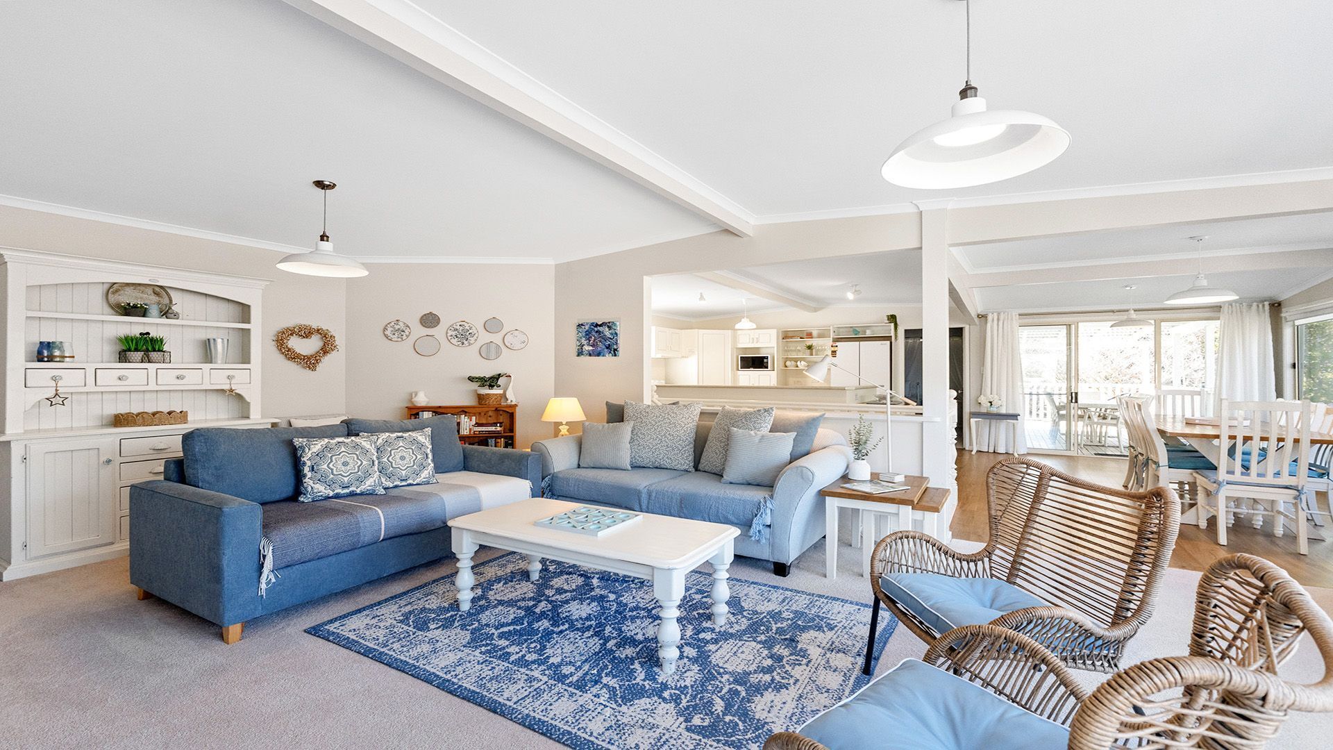 A spacious living room with a blue sofa set, a white coffee table, and wicker chairs.