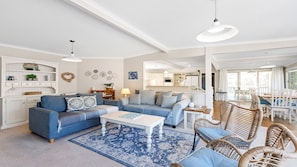 Ein geräumiges Wohnzimmer mit blauem Sofagarnitur, einem weißen Couchtisch und Korbstühlen.