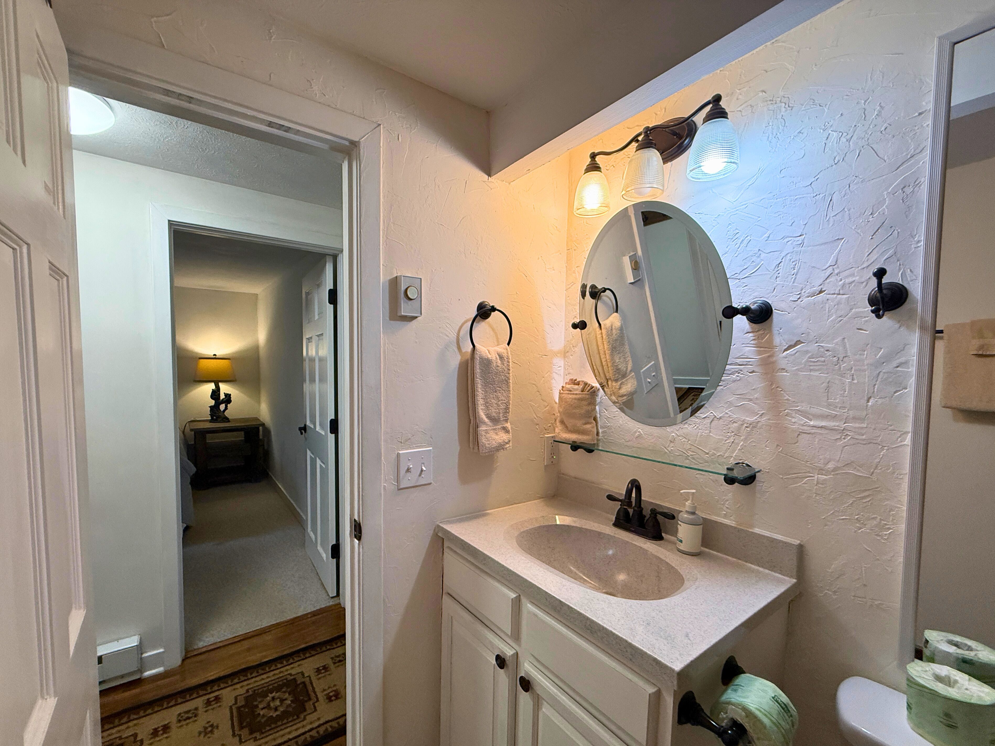 A bathroom with a sink, mirror, towel rack, and a door leading to a hallway.