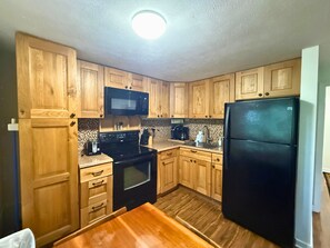A kitchen with wooden cabinets, a black microwave, a black stove, a black refrigerator, and a wooden table. - Cozy Mountain Condo Near Sugar Mountain Ski Resort (Sugar Mountain)