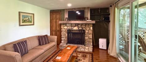 A living room with a sofa, a stone fireplace, a wooden coffee table, and a patterned rug.