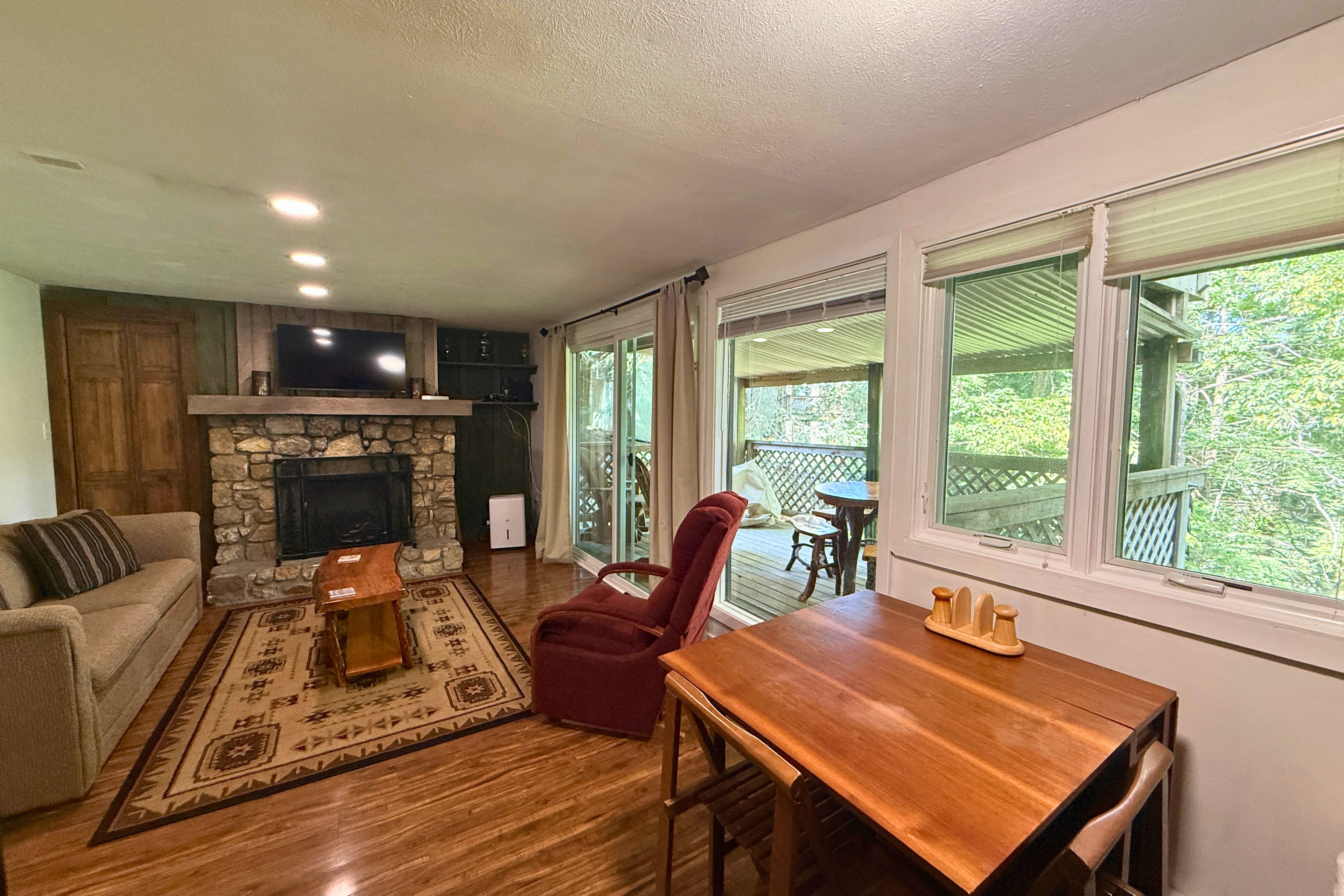A living room with a stone fireplace, a wooden dining table, and a red chair.