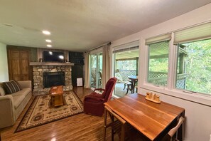 A living room with a stone fireplace, a wooden dining table, and a red chair. - Cozy Mountain Condo Near Sugar Mountain Ski Resort (Sugar Mountain)