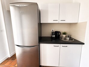 A compact kitchen with a stainless steel refrigerator, a coffee maker, a sink, and white cabinets.