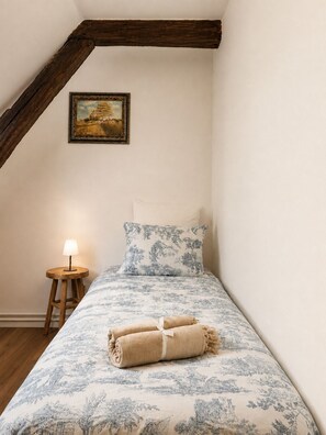 A bedroom with a bed, a nightstand, a lamp, a painting, and a wooden beam structure.