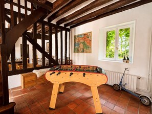A room with a wooden foosball table, a scooter, a map on the wall, and a window with greenery outside.