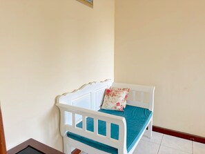 Una cama pequeña blanca con un colchón color aguamarina y una almohada estampada frente a una pared lisa.