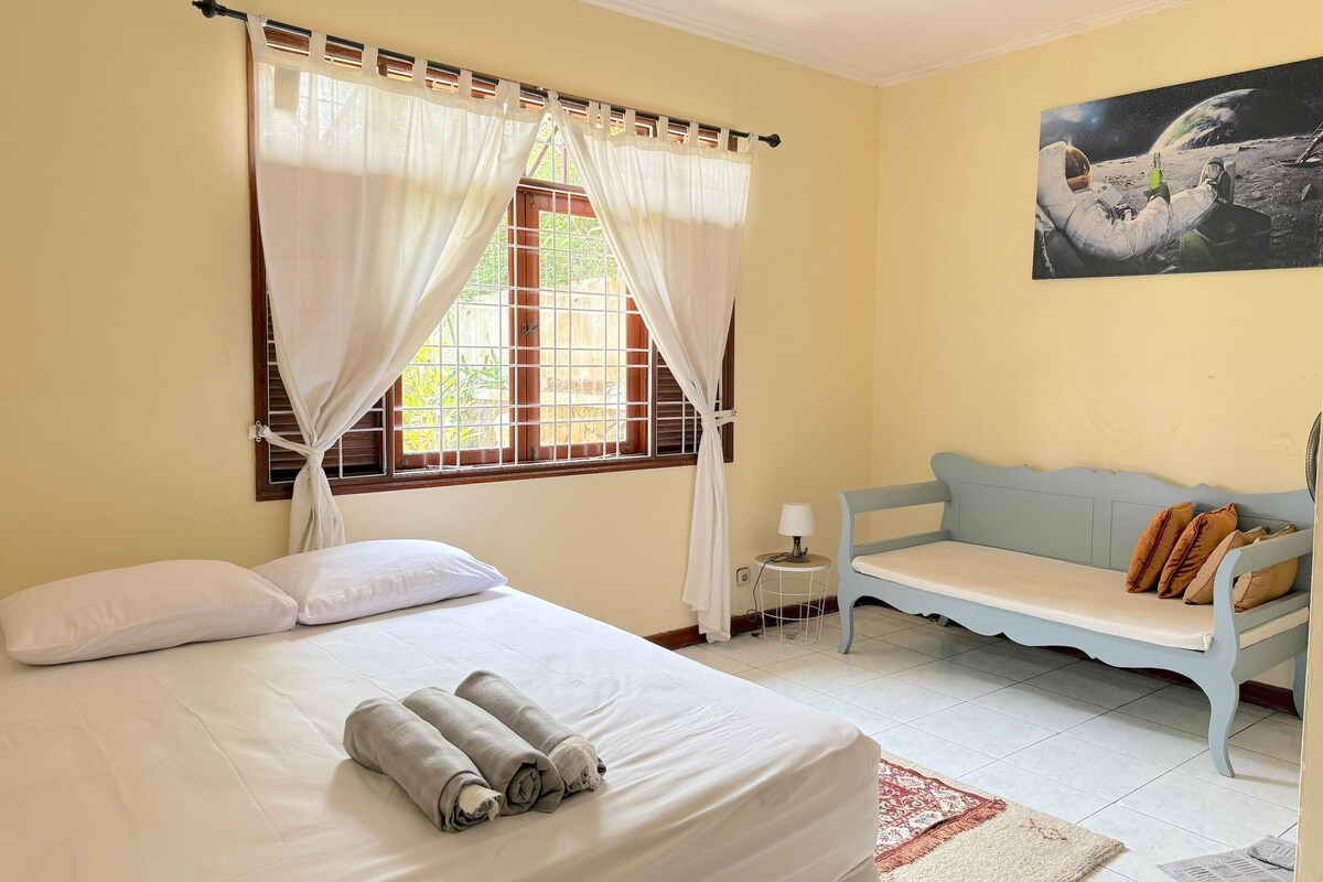 Una habitación de hotel con cama, ventana con cortinas, sofá y un cuadro en la pared.