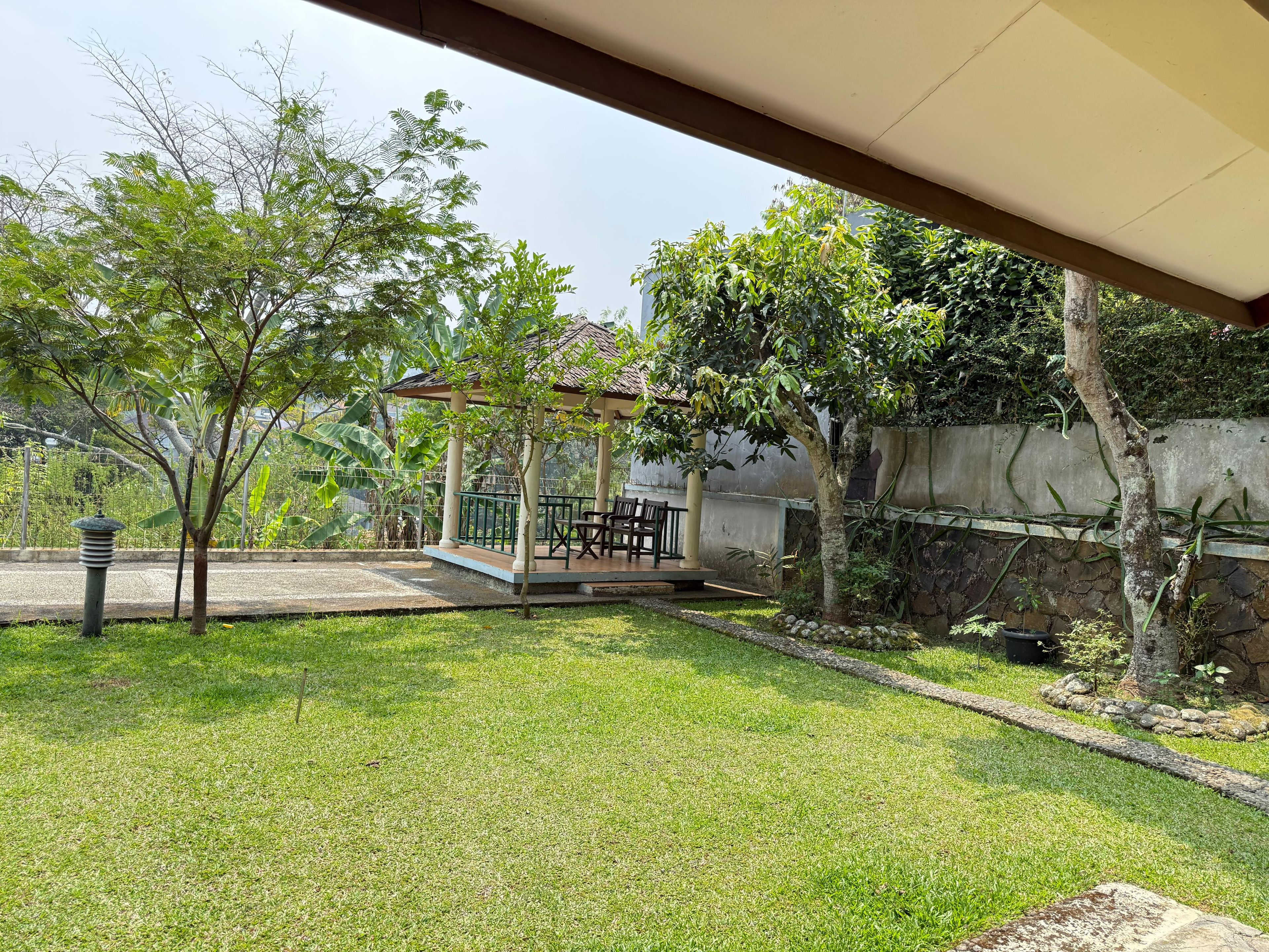 A covered outdoor seating area with a table and chairs, surrounded by a grassy lawn and trees.