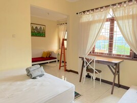 Una habitación con cama, escritorio y silla, ventana con cortinas, un cuadro en la pared y un sofá rojo.